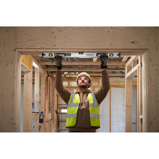 Photo of worker using STANLEY FMHT43674-1 spirit level in wooden construction, holding tool above head for alignment.