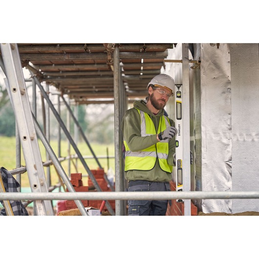 STANLEY FMHT43675-1 spirit level used vertically on a construction site by a worker in a safety vest.