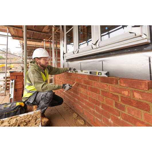 STANLEY FMHT43675-1 spirit level used by a worker to check brick wall alignment at a construction site.