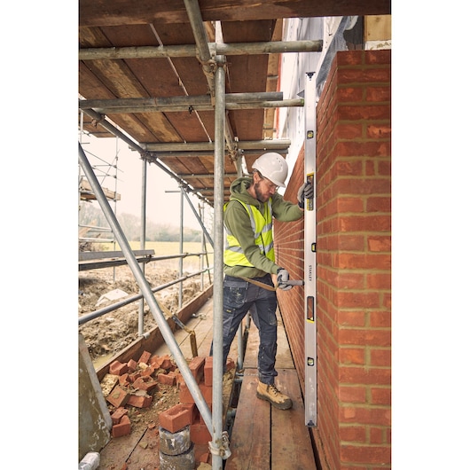 STANLEY FMHT43679-1 spirit level in use by a construction worker checking a brick wall on scaffolding.