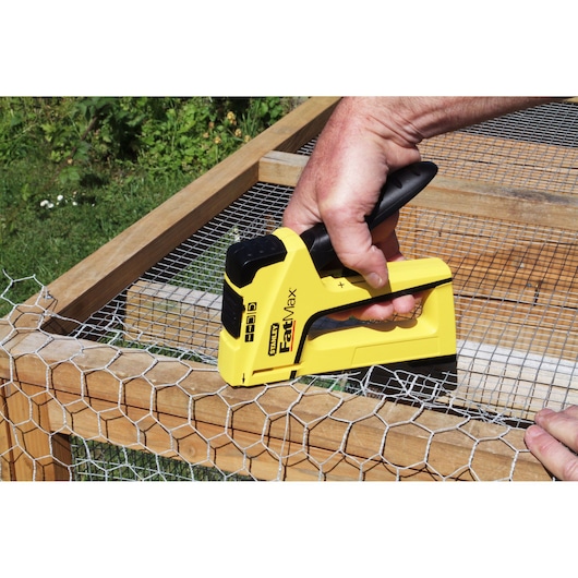 STANLEY FMHT6-70411 staple gun fastening wire mesh to wooden frame outdoors.