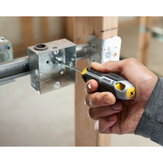 Hand using a STANLEY Phillips screwdriver to tighten a screw in a metal electrical box attached to wood.