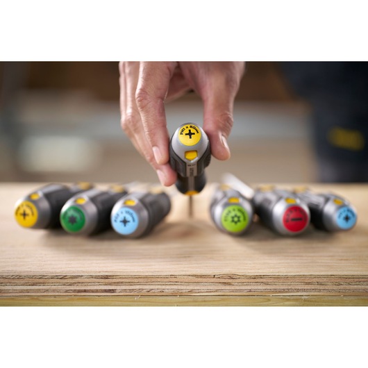 Hand holding a Stanley screwdriver with color-coded handles on a wooden surface.