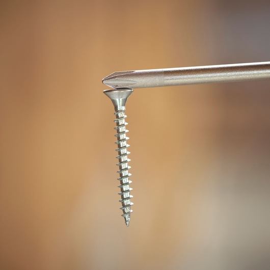 Close-up of a screwdriver tip inserted into the head of a metal screw against a blurred brown background.