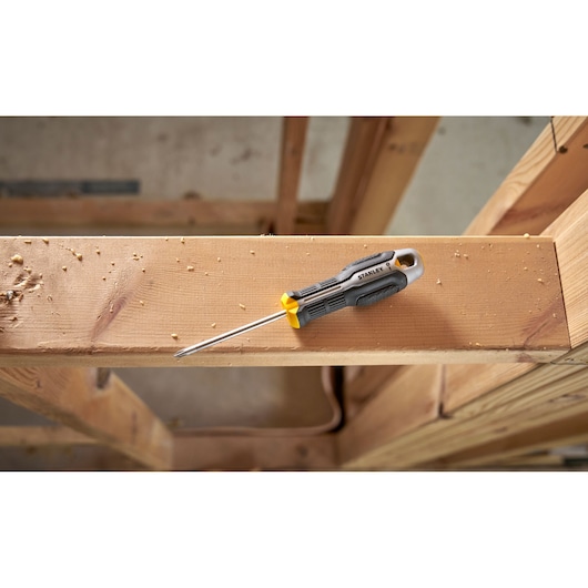 Stanley screwdriver with black and yellow handle resting on a wooden beam in a construction area.