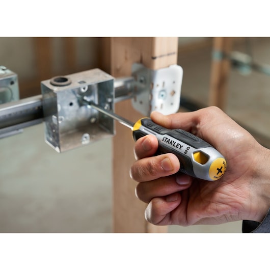 Hand using a STANLEY Phillips screwdriver to fasten a screw in a metal electrical box on a wooden frame.