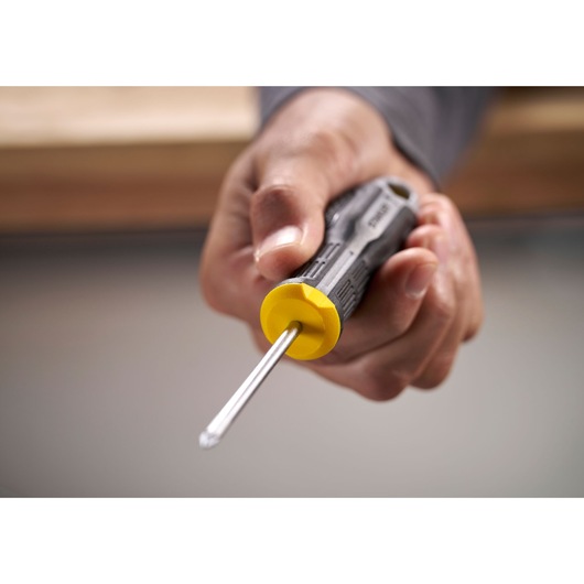 Hand holding a Stanley screwdriver with a yellow and black handle, pointed tip facing forward.