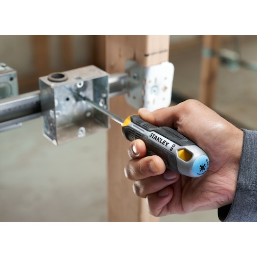 Hand using a STANLEY screwdriver to tighten a screw inside a metal electrical box on a construction site.