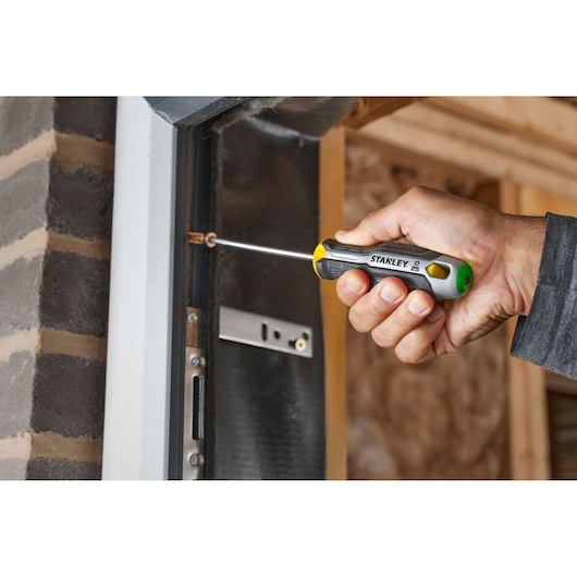 Hand using STANLEY screwdriver to tighten screw in door frame indoors.