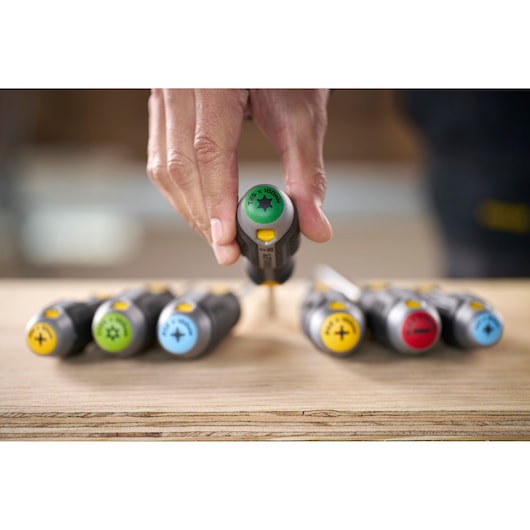 Hand picking a color-coded Stanley screwdriver from a set placed on a wooden surface.