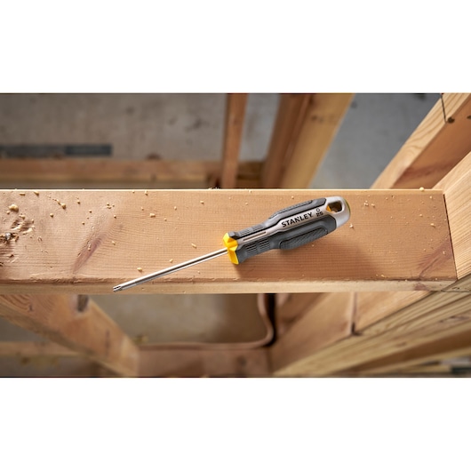 Stanley screwdriver with grey and yellow handle resting on a wooden beam in a construction setting.