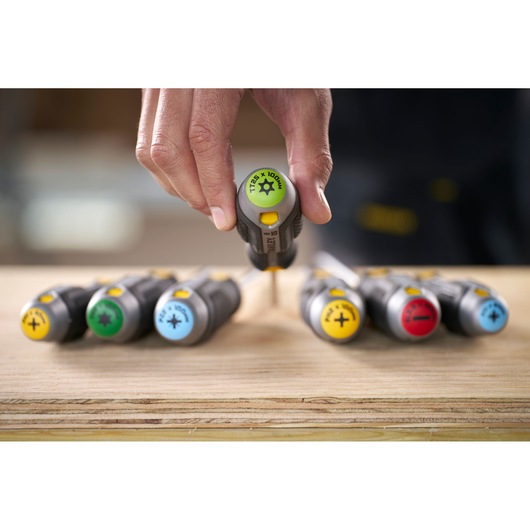 Hand using a STANLEY screwdriver from a set with color-coded handles on a wooden surface.