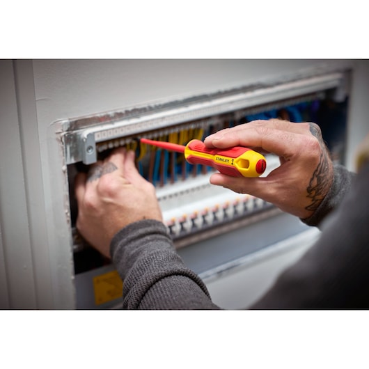 Person uses a STANLEY insulated screwdriver to work on an electrical panel with multiple wires.