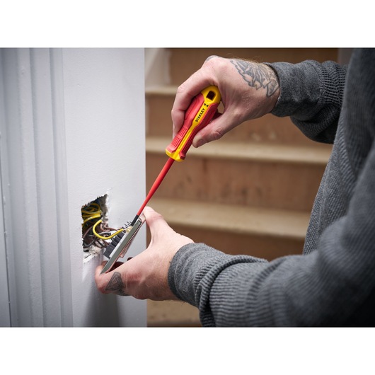 Person uses STANLEY insulated screwdriver to work on electrical wiring in a wall near stairs.