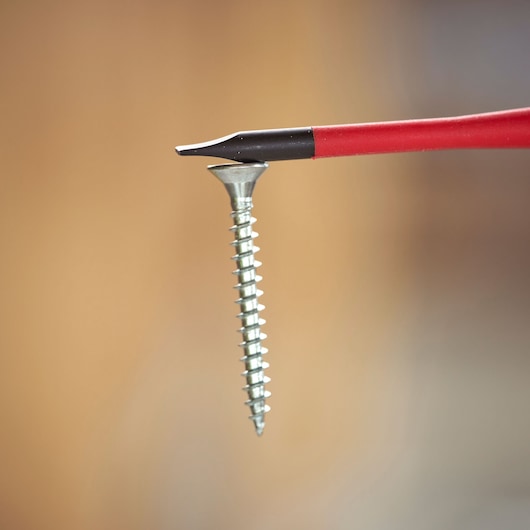 Close-up of a red-handled flathead screwdriver next to a silver screw with blurred background.