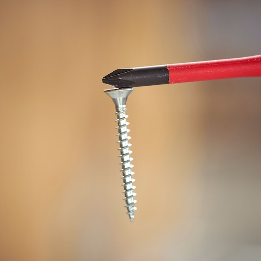 Close-up of a red-handled screwdriver bit engaging a Phillips screw against a plain background.