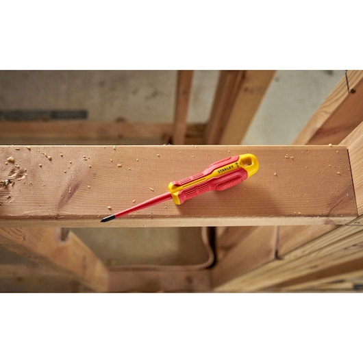 Stanley insulated screwdriver with yellow and red handle resting on a wooden beam at a construction site.