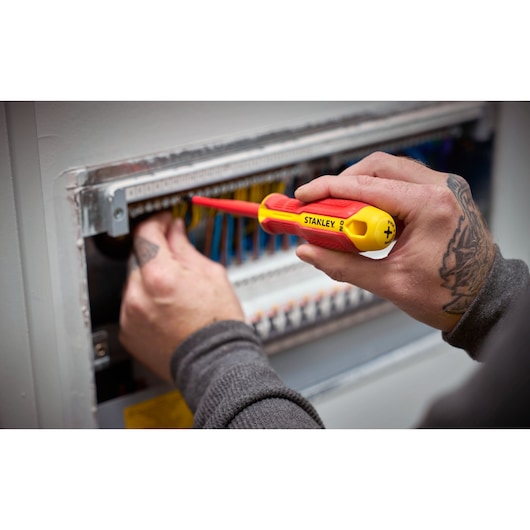 Person uses a STANLEY insulated screwdriver to work on electrical wiring inside a panel.