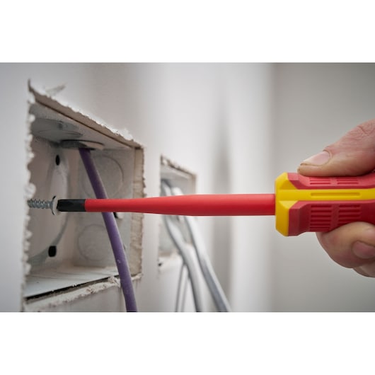 Hand using insulated screwdriver to tighten a screw inside an electrical box with wires visible.