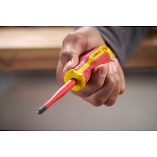 Hand holding a red and yellow insulated STANLEY screwdriver, close-up view of tool tip and handle.