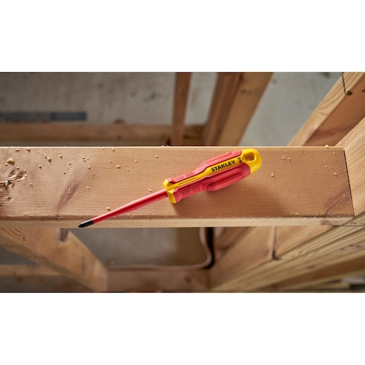 Stanley insulated screwdriver with red and yellow handle lying on a wooden beam at a construction site.