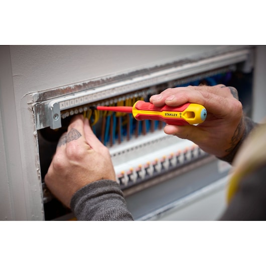 Person uses a STANLEY insulated screwdriver to work on electrical wiring in a control panel.