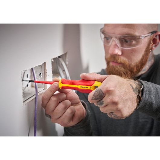 Person uses a STANLEY insulated screwdriver to install or adjust an electrical socket in a wall.