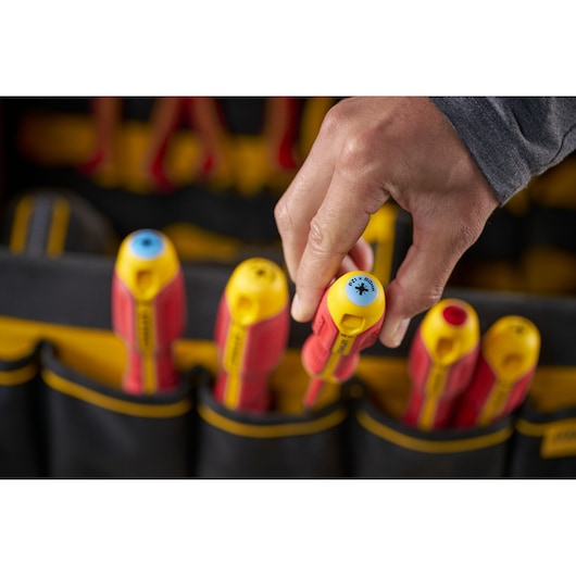 A hand picking a yellow and red insulated screwdriver from a tool pouch with other similar tools visible.