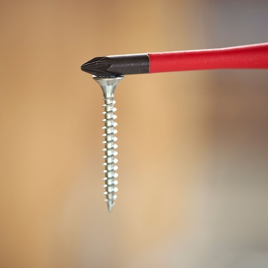 Close-up of a red screwdriver with a Phillips head tip holding a silver screw against a blurred background.