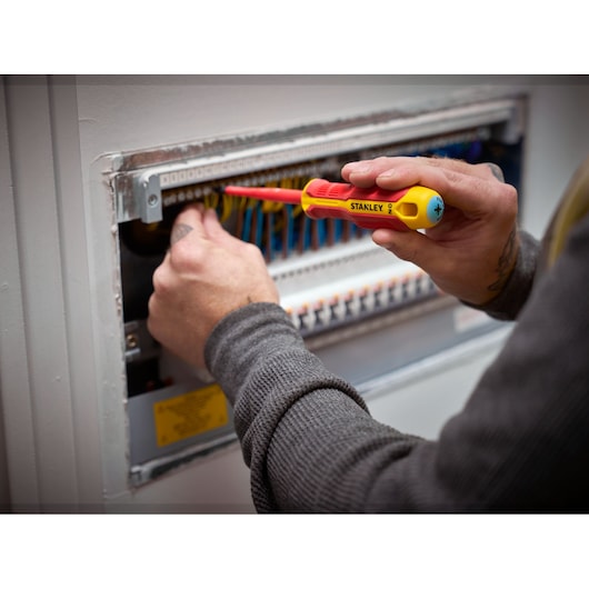 Person uses a STANLEY insulated screwdriver to work on an electrical panel with colorful wires.