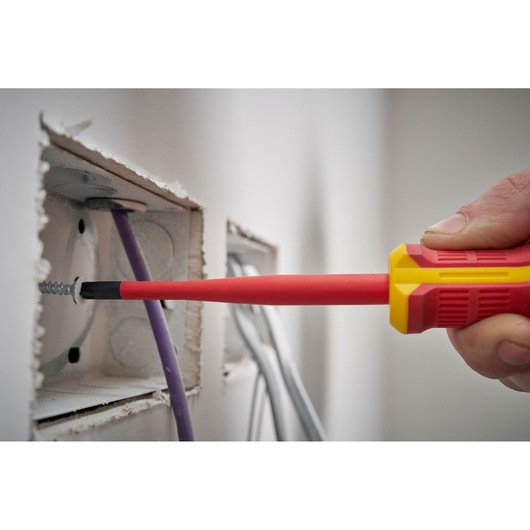 Insulated screwdriver used for electrical work near wires in a wall.