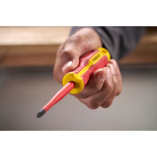 Hand holding a red and yellow STANLEY insulated screwdriver with black tip, close-up view.