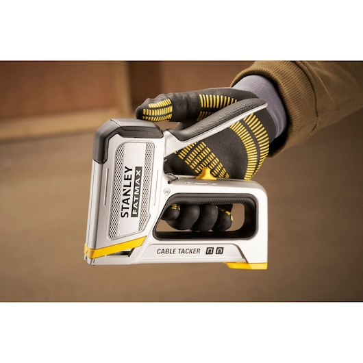 Stanley FMHT70100-0 cable tacker held in gloved hand, silver and yellow, side view.