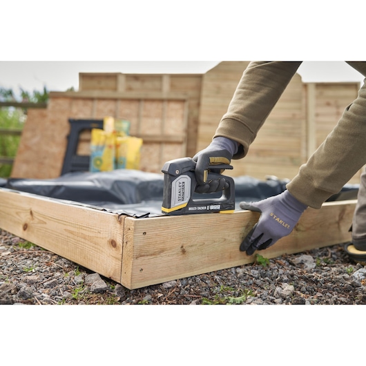 STANLEY FMHT70401-0 hand stapler in use on wooden frame outdoors, close-up of gloved hands.