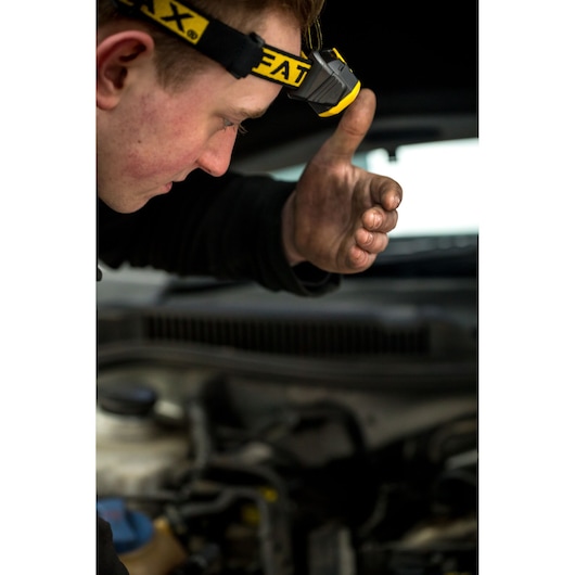 Photo of STANLEY FMHT81509-0 headlamp worn by mechanic with dirty hand near engine.