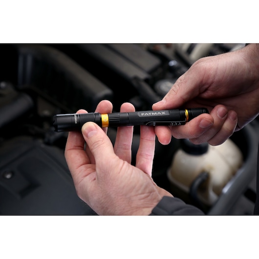 Photo of STANLEY FMHT81510-0 black FatMax flashlight held in hands, shown in an automotive setting.