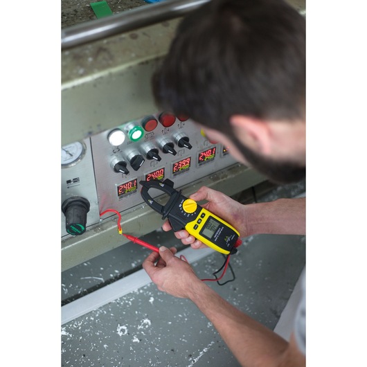 Photo of STANLEY FMHT82564-0 digital clamp meter being used to test voltage on industrial control panel.
