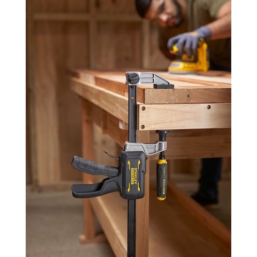 STANLEY FMHT83006-0 bar clamp with yellow and black handle on wooden workbench, side angle photography.