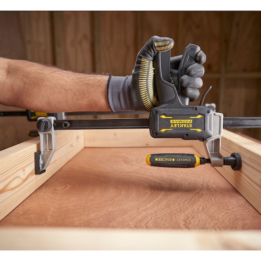 Photo of STANLEY FMHT83007-0 clamp tool securing wood frame, hand in work glove holding handle.