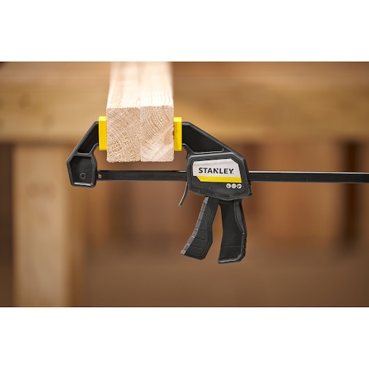 STANLEY FMHT83271-0 trigger clamp holding wooden beam, product side view, woodworking context.