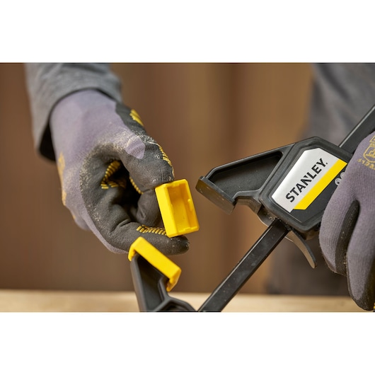 STANLEY FMHT83271-0 bar clamp in use, close-up of gloved hands adjusting yellow jaw pad.