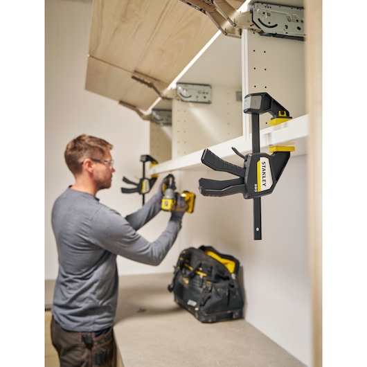 Photo of STANLEY FMHT83273-0 quick grip clamp mounted on white shelf during workshop use.