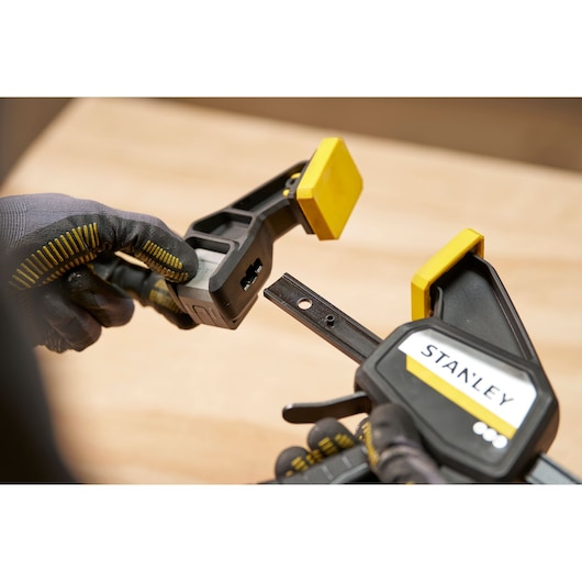 STANLEY FMHT83273-0 trigger clamp closeup, black and yellow, with gloved hands, product photography.