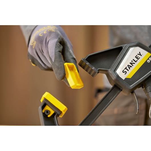 Stanley FMHT83274-0 clamp with removable yellow jaw cover held by gloved hand, side angle photo.