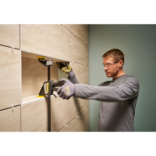 Photo of a worker using a STANLEY FMHT83275-0 clamp to secure tiles during installation on a wall.