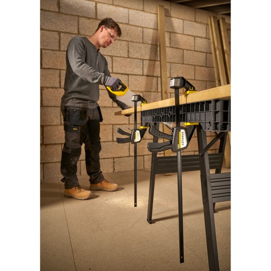 Photo of STANLEY FMHT83276-0 bar clamps securing wood on workbench, used by worker in workshop.