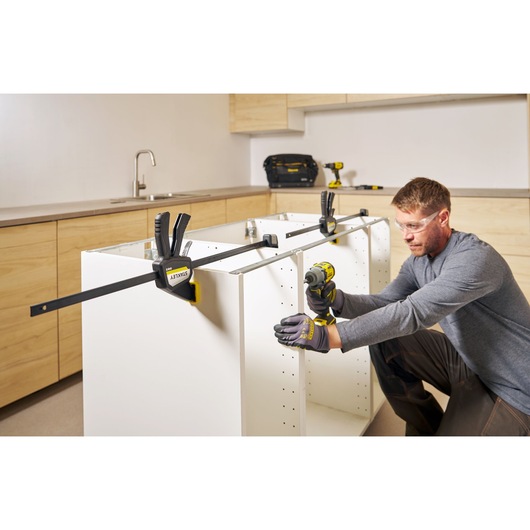 Photo of STANLEY FMHT83276-0 bar clamp securing white cabinet panels during assembly in a modern kitchen.