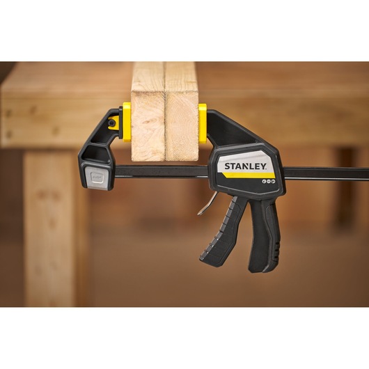 STANLEY FMHT83276-0 bar clamp with black and yellow accents holding two wooden boards, side view.
