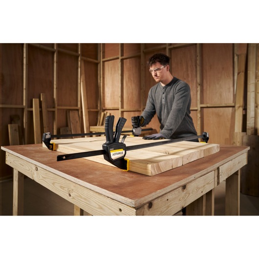 STANLEY FMHT83277-0 bar clamp securing wood pieces on a workbench in a workshop setting.