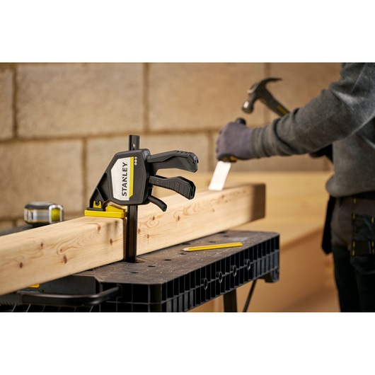 STANLEY FMHT83278-0 clamp secures wood on workbench, close-up photo in workshop with carpenter.